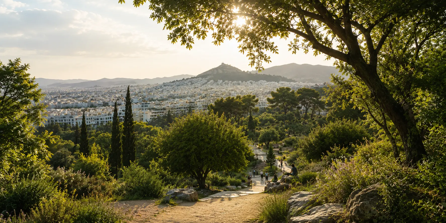 View over the white rooftops of Athens from a tree-shaded hillside path, with a hill rising above the city in the distance and people walking between pines and shrubs.